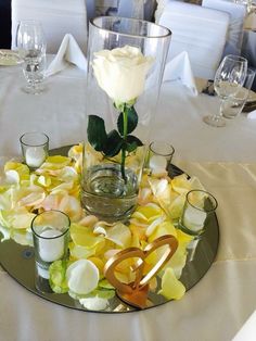 a glass plate topped with flowers and candles on top of a white table cloth covered table