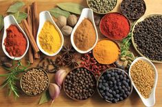 several spoons filled with different types of spices on top of a wooden table next to herbs