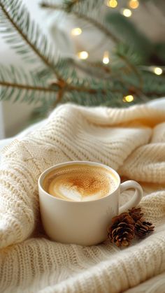 a cup of cappuccino sits on a blanket next to a christmas tree