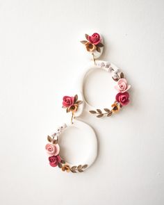 two white hoop earrings with pink flowers and leaves hanging from the front, on a white background