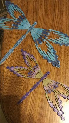 three dragonflys made out of popsicle sticks sitting on top of a wooden table