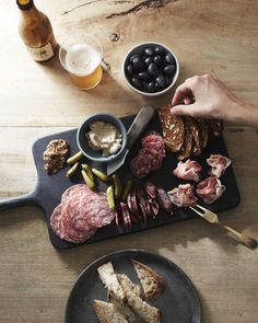 a person is cutting meats on a board with olives and other food items