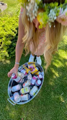 a woman bending over to pick up some drinks from a bucket on the grass in front of her