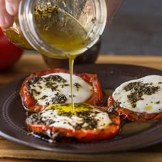 someone is pouring olive dressing over stuffed tomatoes on a plate with other ingredients around them