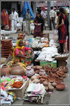 a woman sitting on the ground surrounded by pots and other items in front of her