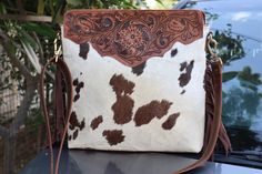 a brown and white cow print purse sitting on top of a car