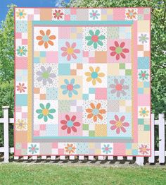 a colorful quilt is hanging on a fence in front of some trees and grass, with the