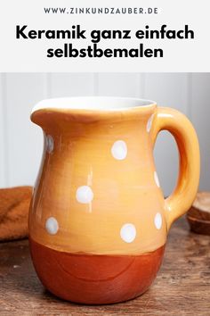 an orange and white vase sitting on top of a wooden table next to a spoon