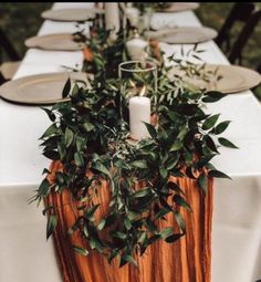 a long table with candles and greenery on it is set for an outdoor dinner