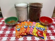 three bags of cereal are sitting on a table next to some bowls and spoons