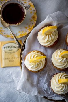 cupcakes with white frosting and lemon slices on a plate next to a cup of tea