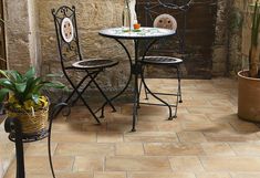 an outdoor table and two chairs sitting next to each other on a tiled patio with potted plants