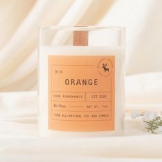 an orange scented candle sitting on top of a white bed next to a small flower