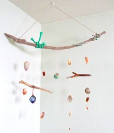 a mobile made out of driftwood and seashells hangs from the ceiling in a white room