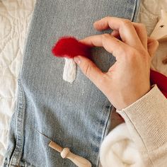 someone is sewing something on a piece of denim with red yarn and wooden pegs