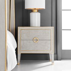 a white lamp sitting on top of a night stand next to a gray and gold bed