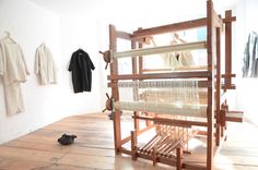 an old weaving machine is sitting in the middle of a room with clothes hanging on the wall