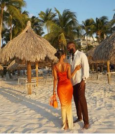 a man and woman standing on the beach with thatched umbrellas in the background