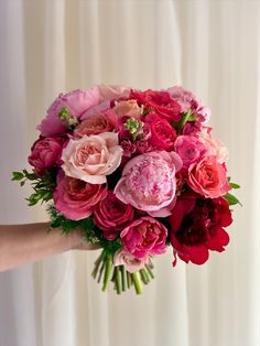 a woman holding a bouquet of pink and red flowers in front of a white curtain