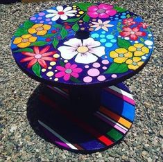 a multicolored table sitting on top of a gravel covered ground with flowers painted on it