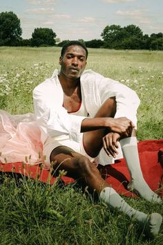 a man sitting on top of a red and white blanket in the middle of a field