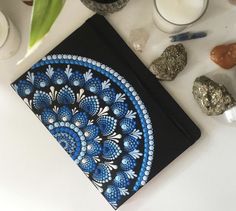 a blue and black notebook sitting on top of a table next to rocks, candles and flowers