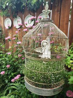 a birdcage with a statue in the middle of it surrounded by pink flowers