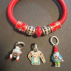 three charms are sitting on a table next to a red rubber bracelet and charm necklace