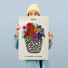 a woman is holding up a poster with flowers in the pot on it's face