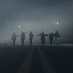 silhouettes of people walking in the dark on a foggy night with street lights