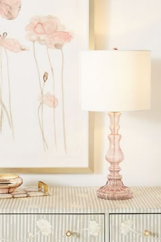 a pink lamp sitting on top of a dresser next to a painting