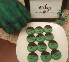 there are many green and black cookies on the plate with faces painted on them next to a framed sign