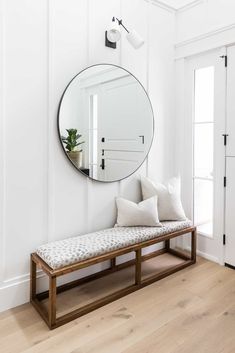 a mirror on the wall above a bench with pillows and a plant in front of it