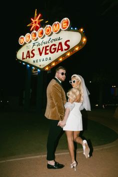 a bride and groom pose in front of the las vegas sign