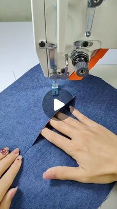 two hands are using a sewing machine to sew on blue material with white stitching