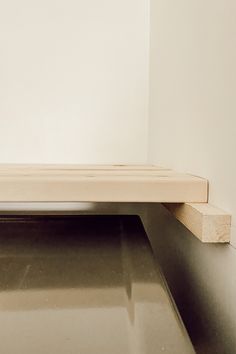 a wooden bench sitting on top of a metal floor next to a white wall in a room