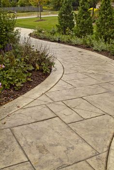 a stone path in the middle of a park with trees and flowers on either side