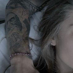 a woman laying in bed with tattoos on her arm