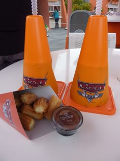 two orange cones sitting on top of a white table next to some dipping sauces