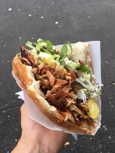 a hand holding a sandwich with meat, lettuce and other toppings on it