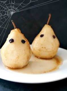 two pears on a white plate with spider web in the middle and one has chocolate eyes