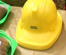 a yellow hard hat sitting on top of a table next to green plastic bowls filled with food