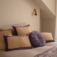 a bed topped with lots of pillows next to a wall mounted light and window sill