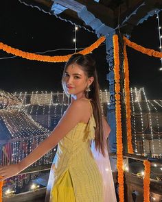 a woman in a yellow dress standing on a balcony with lights and garlands around her