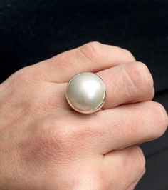 This elegant and stately pearl ring is made from a beautiful and unique white cream 14mm Mabe South Sea AAA Pearl that has many hues including pink. The pearl has been set in sterling silver with a sterling silver ring band handmade from half dome wire. This ring has some height, the setting is almost 1/2 inch high. The white cream pearl is more matte than the other mabe pearls listed, but still has a luminescent quality that makes it captivating! Made to order! Choose your size and your color p Classic Mother Of Pearl Round Rings, Classic Mother Of Pearl Rings, Formal Mother Of Pearl Round Ring, Elegant Round Mother Of Pearl Ring, Wedding Pearl Ring In Mother Of Pearl, Formal Round Mother Of Pearl Ring, Wedding Pearl Ring With Mother Of Pearl, Formal Mother Of Pearl Ring, White Mother Of Pearl Wedding Ring