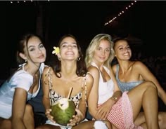 three women sitting next to each other with drinks in their hands and one holding a coconut