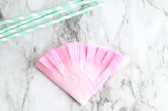 two straws and a pink paper fan on a marble surface with mint green striped straws