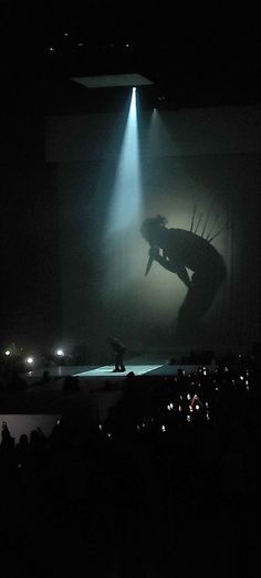 a person standing in front of a stage with a light shining down on him and his arm outstretched