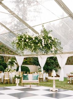 an outdoor wedding reception setup with white flowers and greenery on the ceiling, set up in a tented area