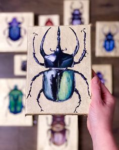 a hand holding up a small wooden block with a beetle painted on it